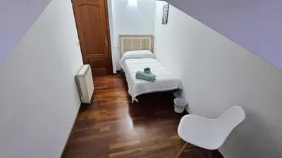 a small room with a bed and a white chair at Garcia Prieto Vivienda in Santiago de Compostela
