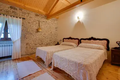 a bedroom with two beds and a stone wall at Casa Rural A Avoa María in Campo Lameiro