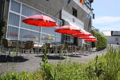 a row of tables and chairs with red umbrellas at Albergue Ferramenteiro in Portomarin
