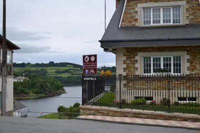 a house with a sign in front of a river at Albergue Ferramenteiro in Portomarin