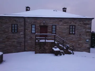 a brick building in the snow with a bench in front at Apartamentos rurales Casa Do Cabo in Vega de Logares