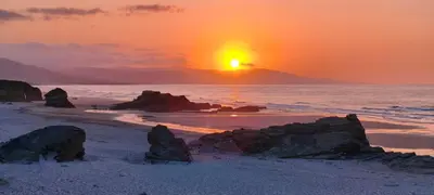 a sunset on a beach with rocks in the sand at Balea House in Barreiros