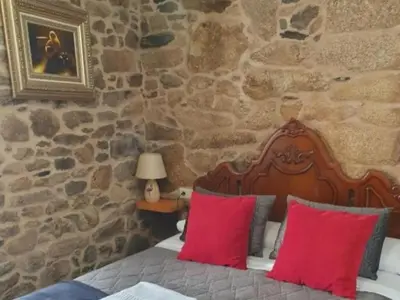 a bedroom with a bed with red pillows and a stone wall at La pallota de san Cristóbal in Camino