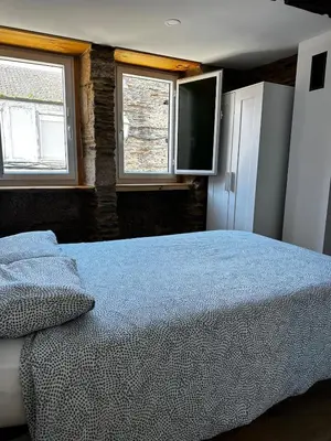 a bedroom with a bed and a tv and two windows at A Casiña da Ponte in Lugo