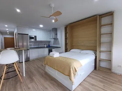 a bedroom with a large white bed and a kitchen at Precioso loft para disfrutar de Ourense in Ourense