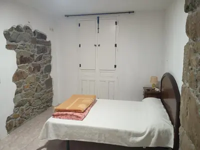 a bed in a room with a stone wall at Habitaciones Rurales Los Semellones in La Llama