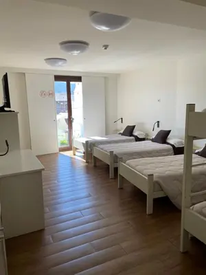 a group of beds in a room with white sheets at Albergue Guiana in Ponferrada
