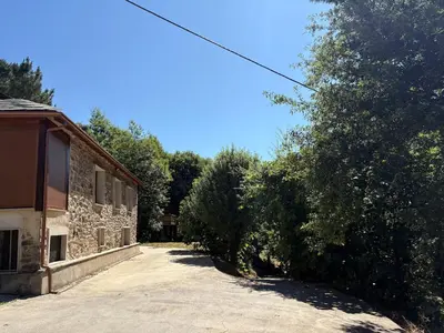 a driveway leading to a stone building with trees at Vivienda turística en plena naturaleza O Poleiro
