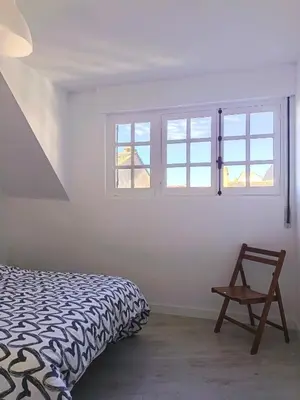 a bedroom with a bed and a chair and windows at Apartamento Maruja Mallo in Viveiro