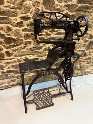 a black antique sewing machine on a stand in front of a stone wall at Adiva A Zapataría in Puentedeume