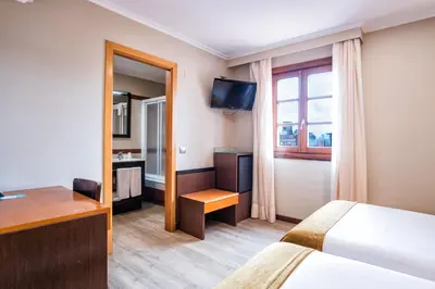 a hotel room with a bed and a desk and a television at Hotel Alda Bonaval in Santiago de Compostela