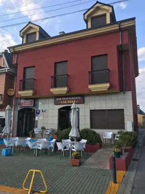 a red building with tables and umbrellas in front of it at Hostal Las Eras in Cubillos del Sil