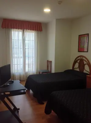 a bedroom with two beds and a desk with a laptop at Hostal Las Eras in Cubillos del Sil