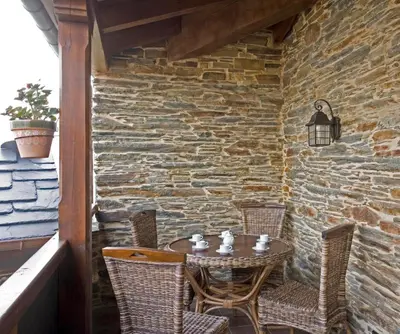 a table and chairs on a patio with a stone wall at Balcón de Oscos in Santa Eulalia de Oscos