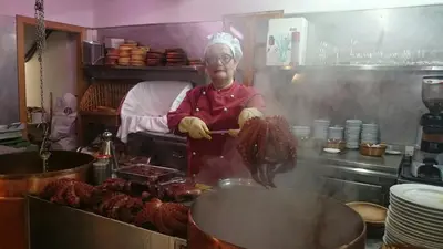 a woman is cooking meat in a kitchen at Apartamento Viveiro, Terraza Grande, 2 dormitorios 2 baños, piscinas, parking, tenis, club social in Jove