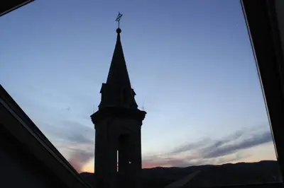 a clock tower with a steeple in front of a sunset at Hostal Siglo XIX in Cacabelos