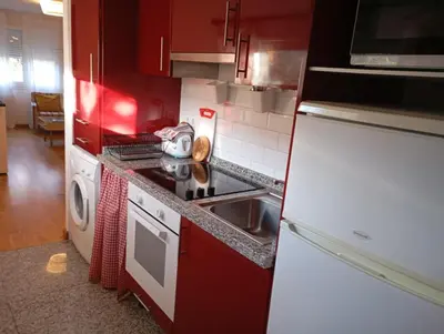 a kitchen with red cabinets and a sink and a refrigerator at Apartamentos el Camino in Villafranca del Bierzo
