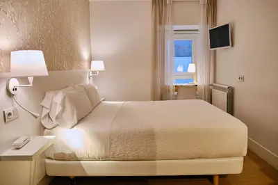 a bedroom with a white bed and a window at Hostal Suso in Santiago de Compostela