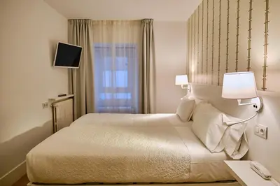 a bedroom with a bed with two lamps and a window at Hostal Suso in Santiago de Compostela