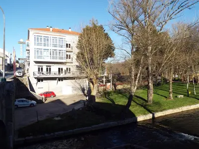 a building next to a river with trees and a building at Hotel Ansuiña in Baños de Molgas