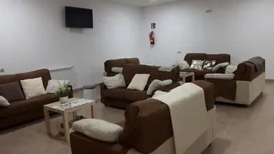 a living room with brown couches and a tv at Albergue O Trisquel in O Pedrouzo