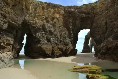 an arch in a rock wall on a beach at Coto Real in Rábade