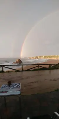 a rainbow over a beach with a bench and the ocean at Hostal Restaurante Parajes in Castropol