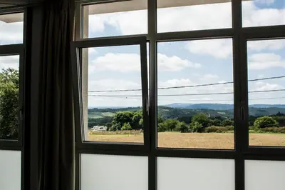 a window with a view of a field and mountains at De Camino in Arzúa