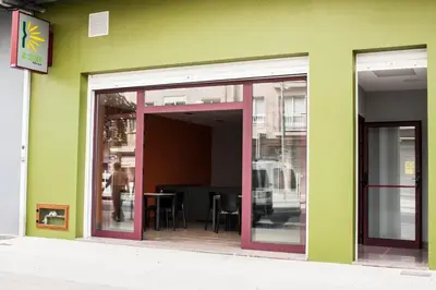 a green building with sliding glass doors and a table at De Camino in Arzúa