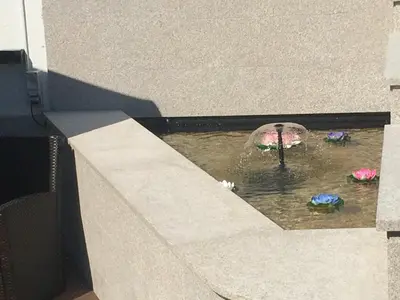 a fountain with an umbrella in a pond with flowers at A Fontana de Luxo Apartamentos in Portomarin