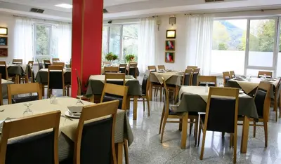 a dining room with tables and chairs and windows at Hotel Valcarce Camino de Santiago in La Portela de Valcarce
