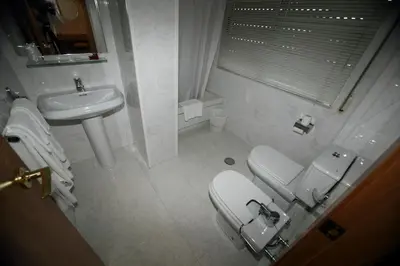 a white bathroom with a toilet and a sink at Hotel Ramos in Silleda