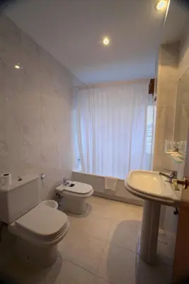 a white bathroom with a toilet and a sink at Hotel Ramos in Silleda