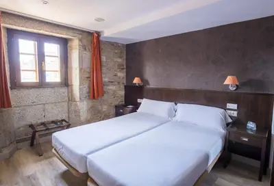 a bedroom with a large white bed and two windows at Hotel Alda Algalia in Santiago de Compostela