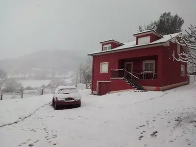 a red house with a car parked in the snow at Casa do Xastre in Baralla