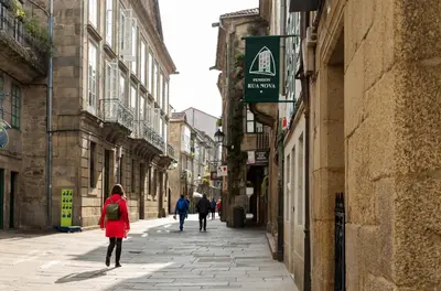 a woman in a red coat walking down a street at Pensión Rua Nova in Santiago de Compostela