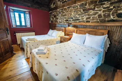 a bedroom with two beds and a stone wall at Apartamentos Rurales Casa Riveras in Santa Eulalia de Oscos