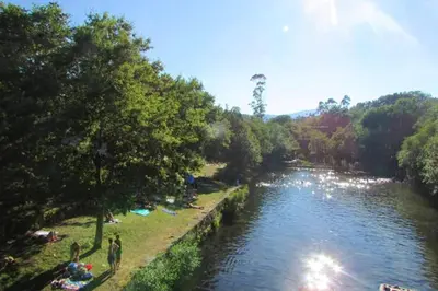 a river with people sitting on the grass next to it at Elegant House in Pontevedra + Private Pool in Rífrío