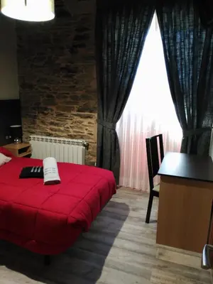 a bedroom with a red bed and a desk and a window at Albergue Pension Porta Santa in Baleira