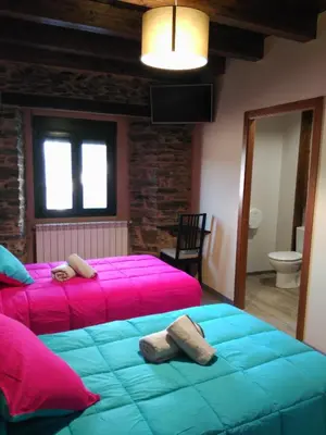 two beds in a room with pink and blue at Albergue Pension Porta Santa in Baleira