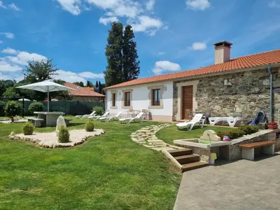 a garden with a stone house and chairs and an umbrella at Pensión Ribadiso in Arzúa