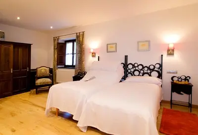 a bedroom with two beds with white sheets and a chair at Hotel y apartamentos rurales L'Anceo in Cibuyo