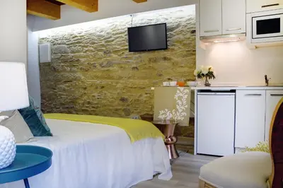 a bedroom with a white bed and a kitchen at Numa Rúa Travesa in Santiago de Compostela