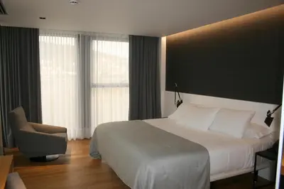 a bedroom with a white bed and a chair and windows at Hotel U Viveiro in Viveiro