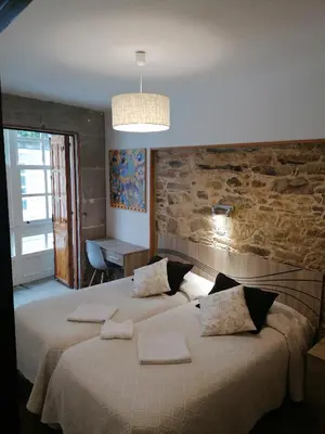 two beds in a bedroom with a stone wall at Hostal Forest in Santiago de Compostela