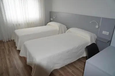 two beds in a hospital room with white sheets at Pension Perez in Portomarin