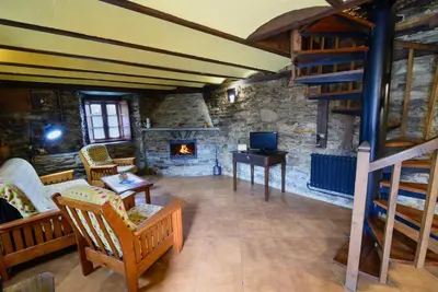 a living room with a stone fireplace and a staircase at Apartamentos Casa de Riba in Teijeira