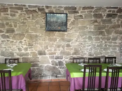 a dining room with two tables and a stone wall at Os Arroxos in Trabadelo