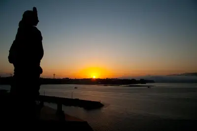 a person standing on a bench watching the sunset at Mirador Ría de Ribadeo in Ribadeo