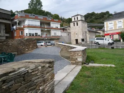 a stone wall in a village with a church at Albergue El Paso in Vega de Valcarce